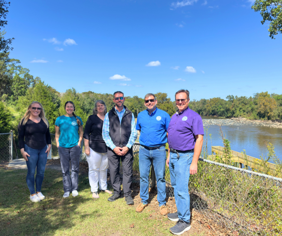 Six people standing outside in front of water